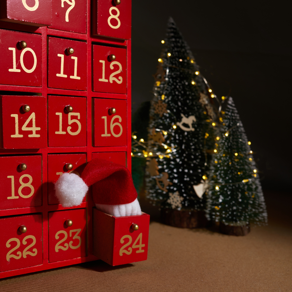 Red advent calendar with numbered drawers and Santa hat, festive Christmas trees in background