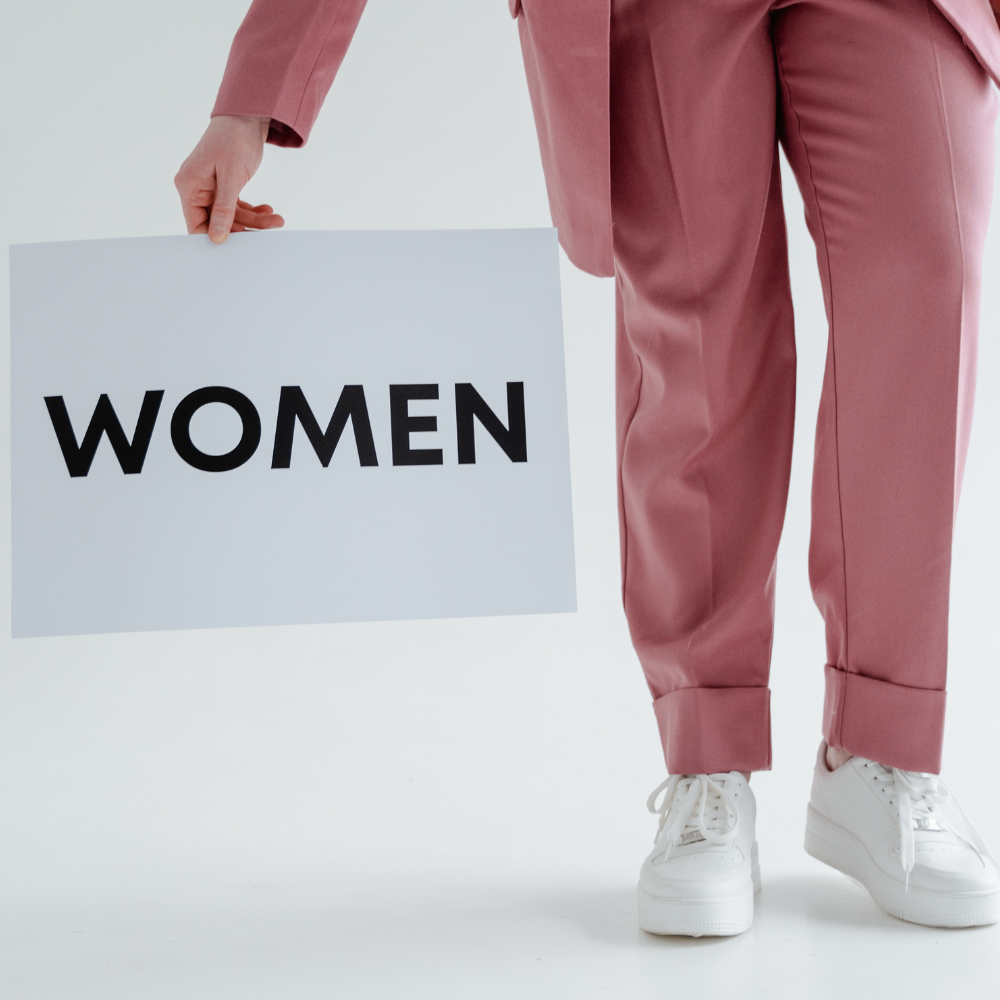 Person in pink suit holding white sign with 'WOMEN' text, white background