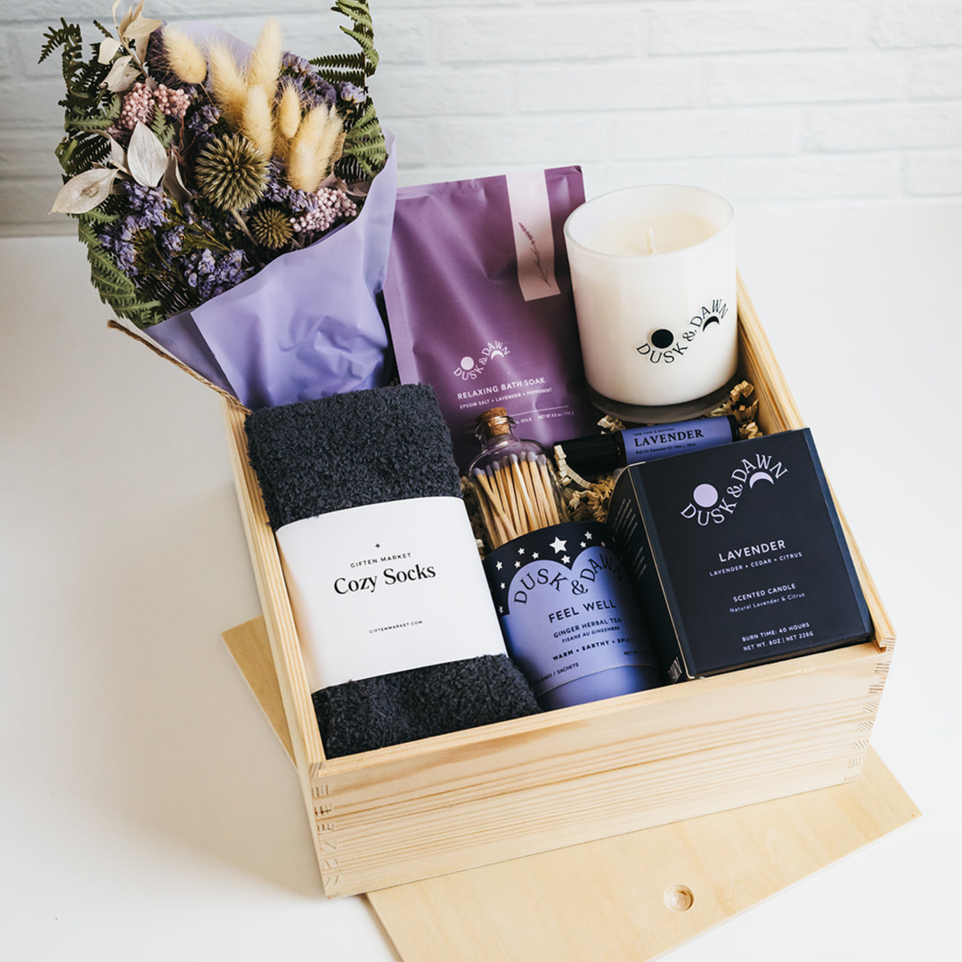 Wooden gift box with candle, socks, bath soak, dried flowers, matches, and self-care items