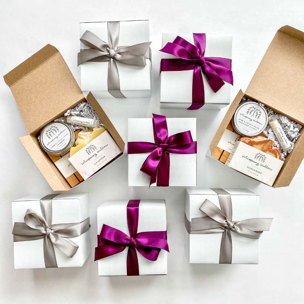 Premium white gift boxes with satin ribbons, filled with candle, soap, snacks, and skincare items
