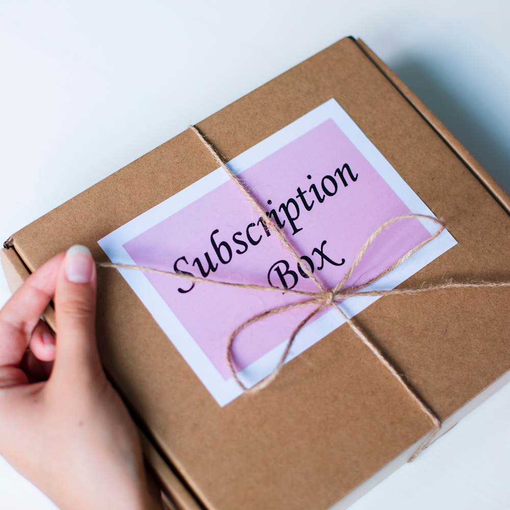 Brown subscription gift box with twine and a pink label being unwrapped by hand