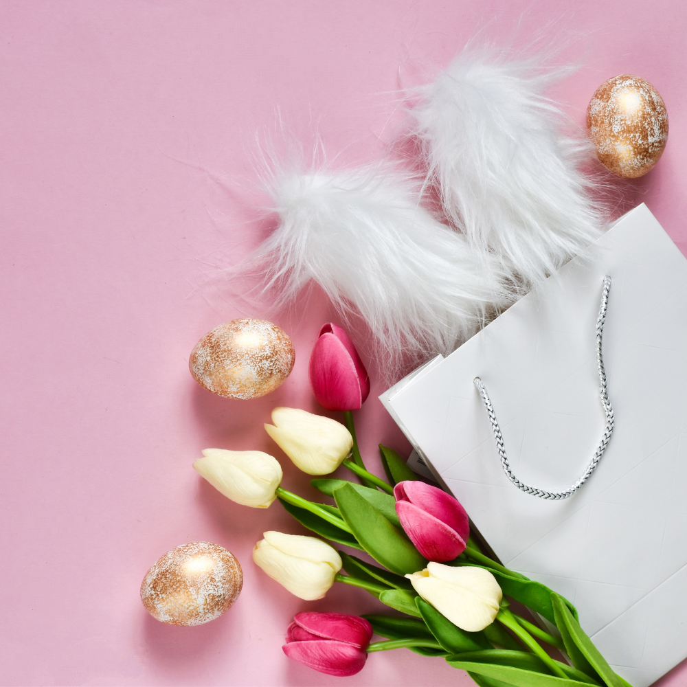 White gift bag with tulips, glitter eggs, and faux bunny ears on pink background