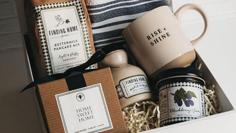 White gift box with pancake mix, striped towel, mug, candle, maple syrup, and blackberry jam