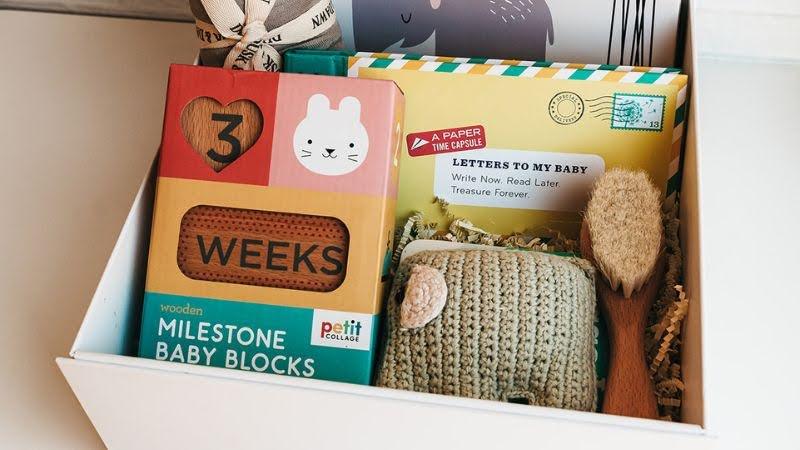 White gift box with milestone baby blocks, baby brush, knit rattle, and baby shower keepsakes