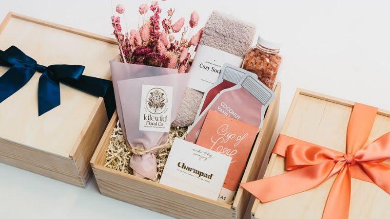 Wooden gift box with dried flowers, cozy socks, bath salts, beverage mix, and notepad