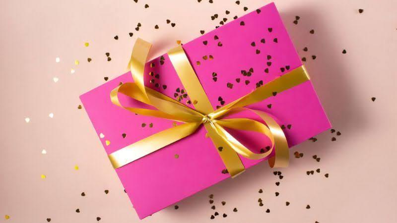 Pink gift box with gold ribbon and heart-shaped confetti on a light background