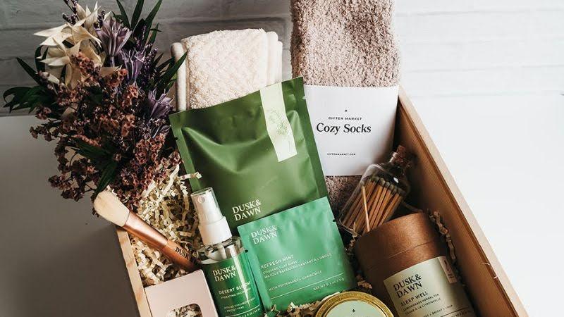 Wooden gift box with cozy socks, spa products, towel, dried flowers, and snacks