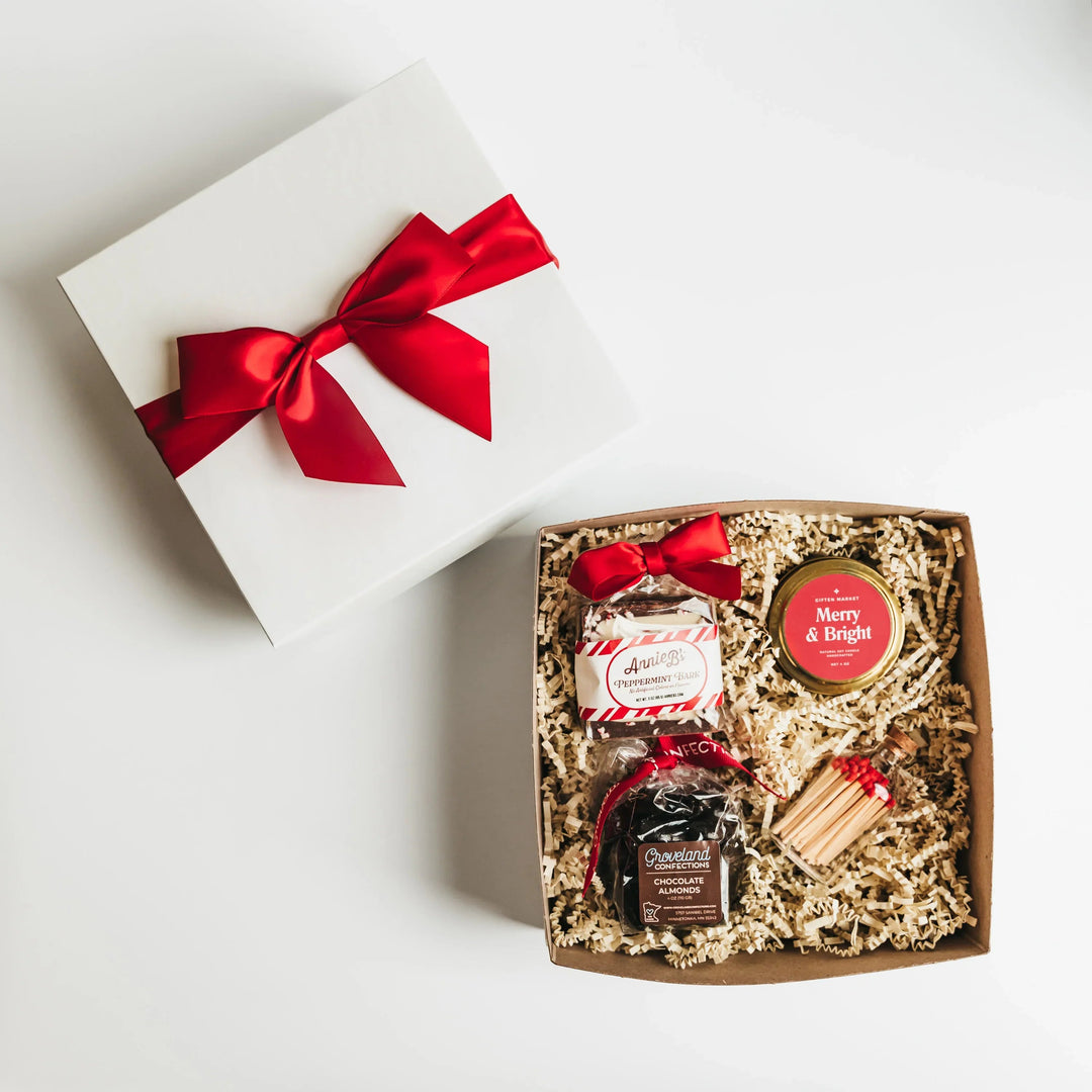 Holiday gift box with red ribbon, candle, chocolate almonds, peppermint bark, and matches