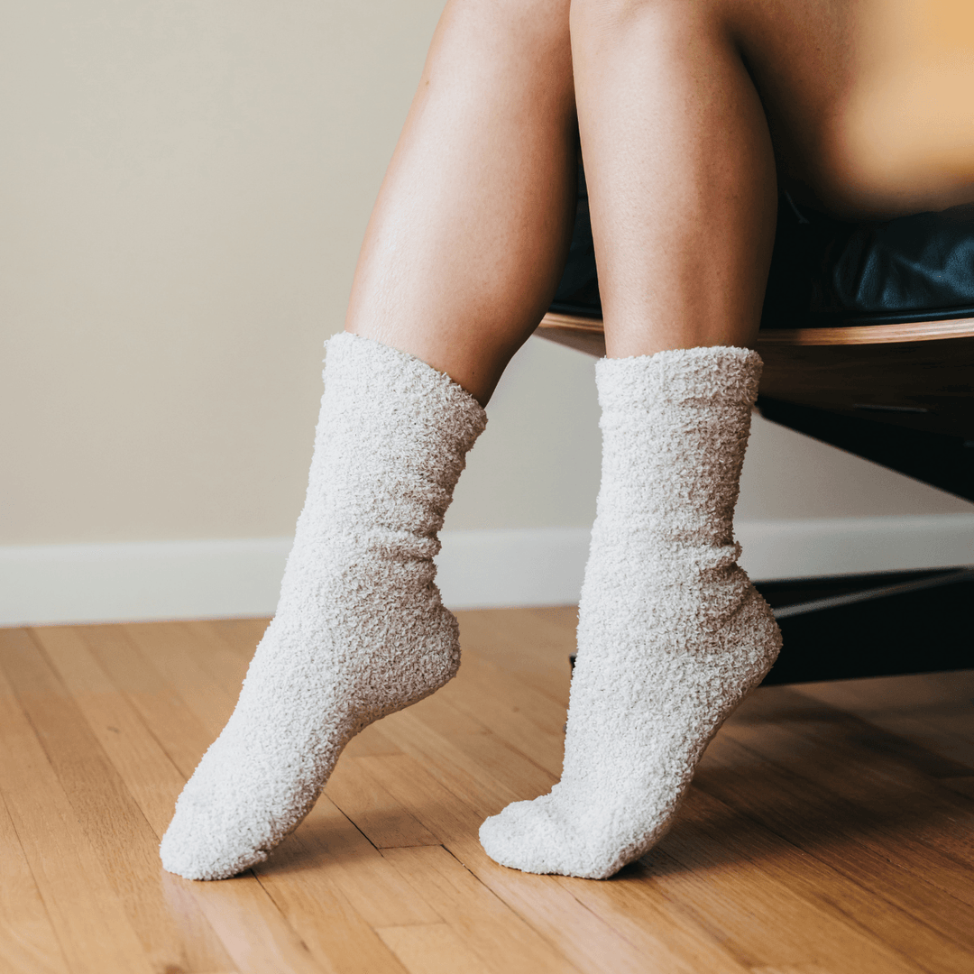 Person wearing cozy ivory plush socks, feet resting on wood floor near modern chair