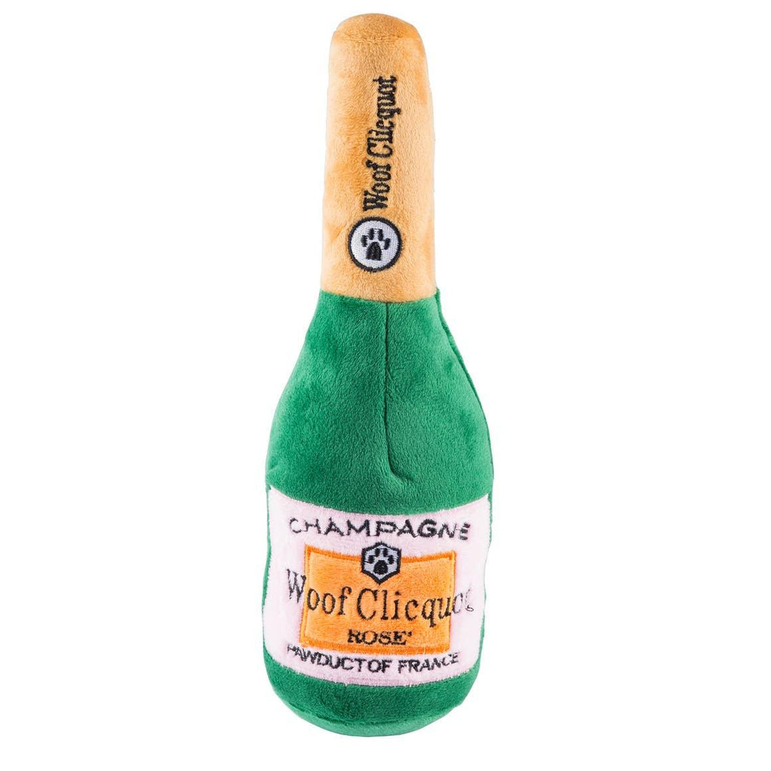 Plush dog toy shaped like a green champagne bottle with embroidered label and gold top