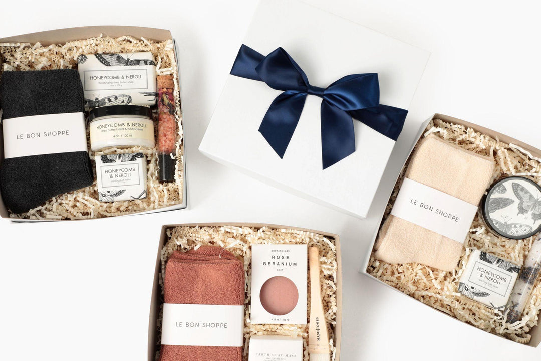 Curated gift boxes with cozy socks, soap, candles, self-care items, and a white box with navy ribbon