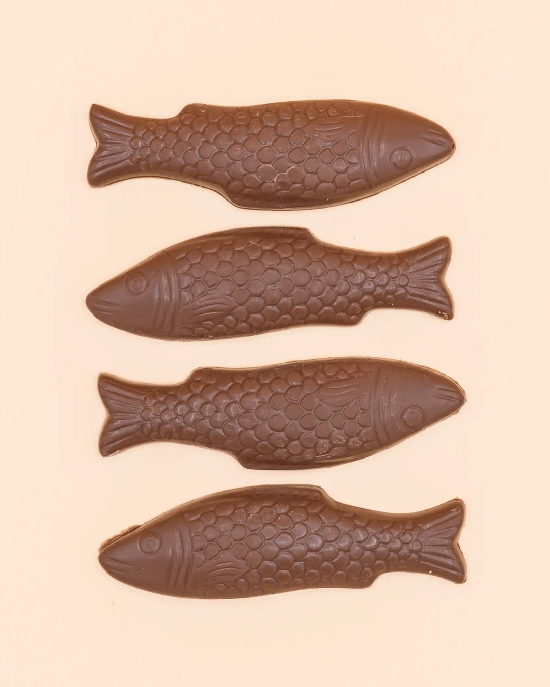 Four milk chocolate fish laid out in a row on a peach background