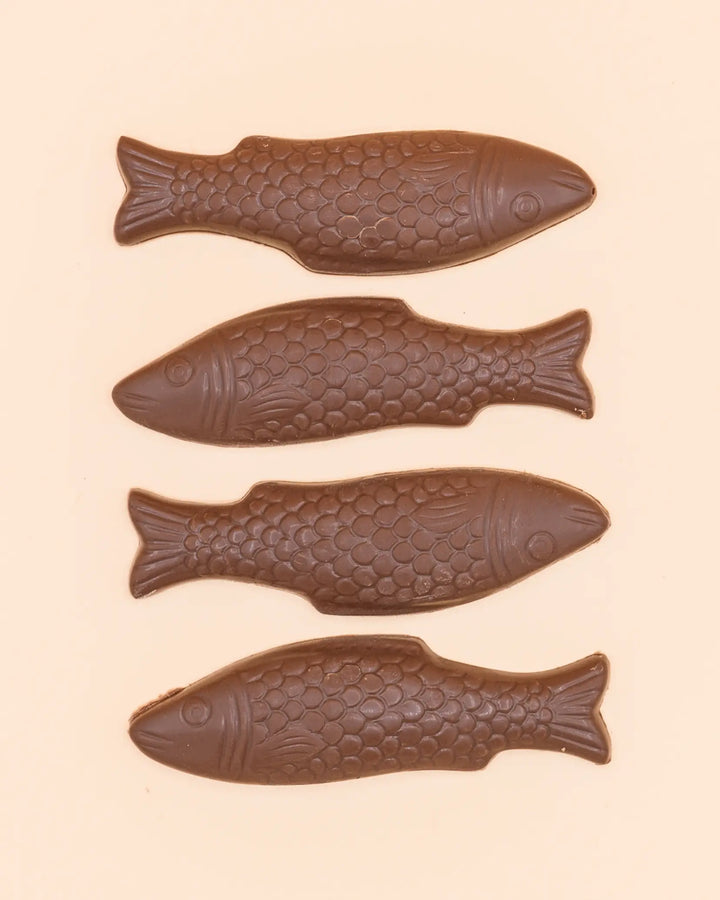 Four milk chocolate fish laid out in a row on a peach background