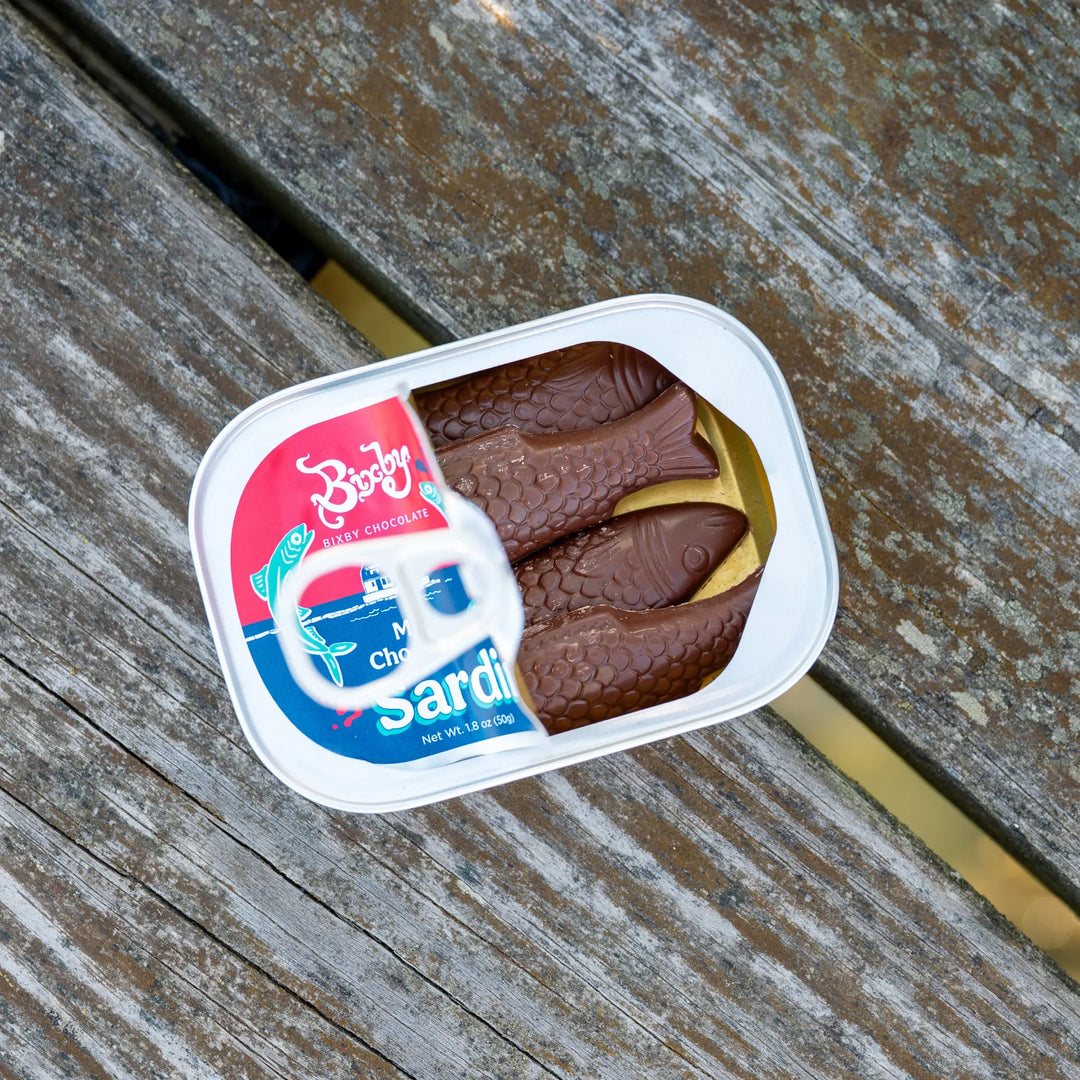 Open Milk Chocolate Sardines tin showing chocolate fish inside, on weathered wood