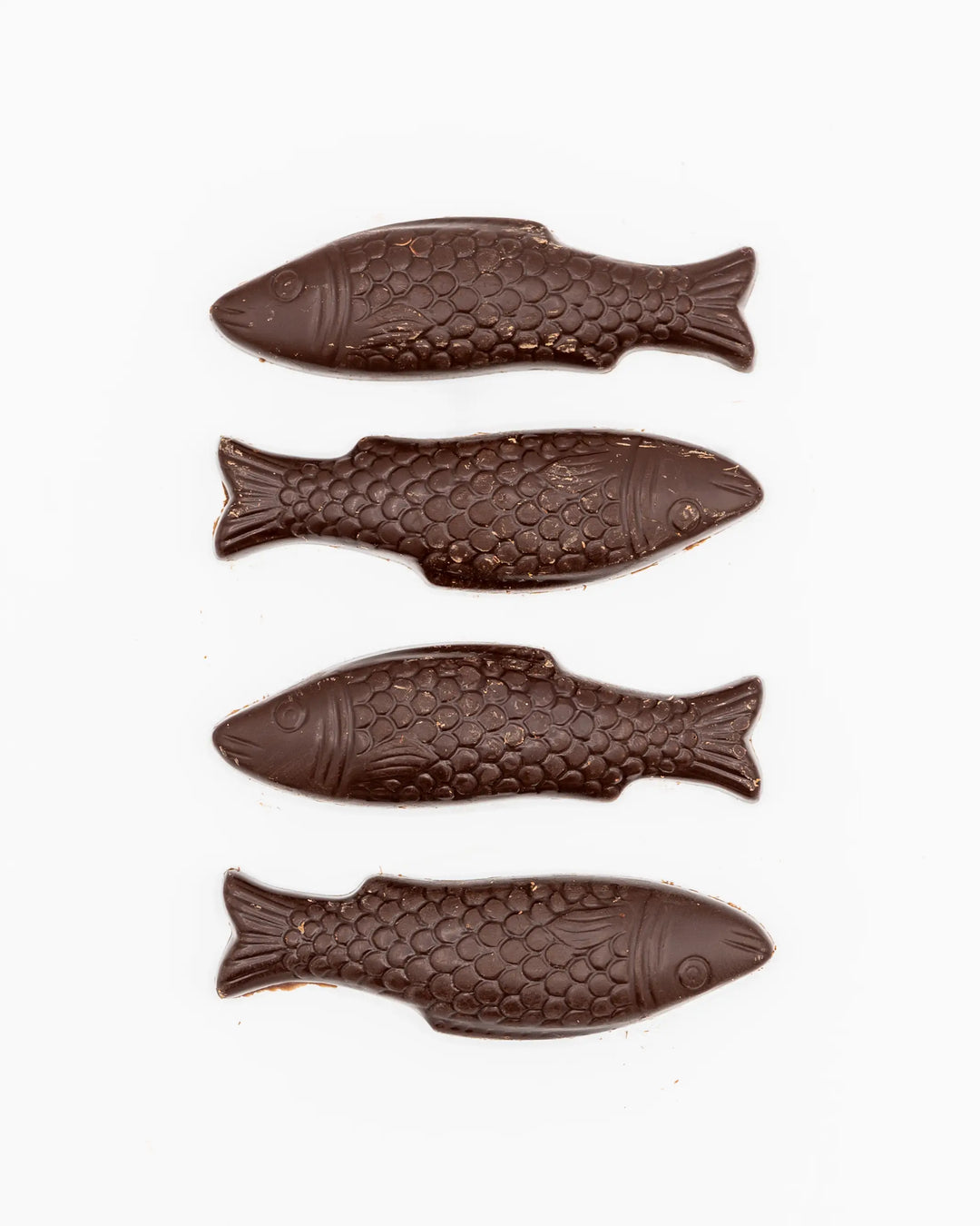 Four dark chocolate fish laid out in a row on a white background