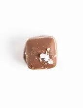 Single milk chocolate caramel topped with sea salt flakes on a white background
