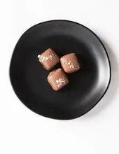 Three milk chocolate sea salt caramels on a black plate