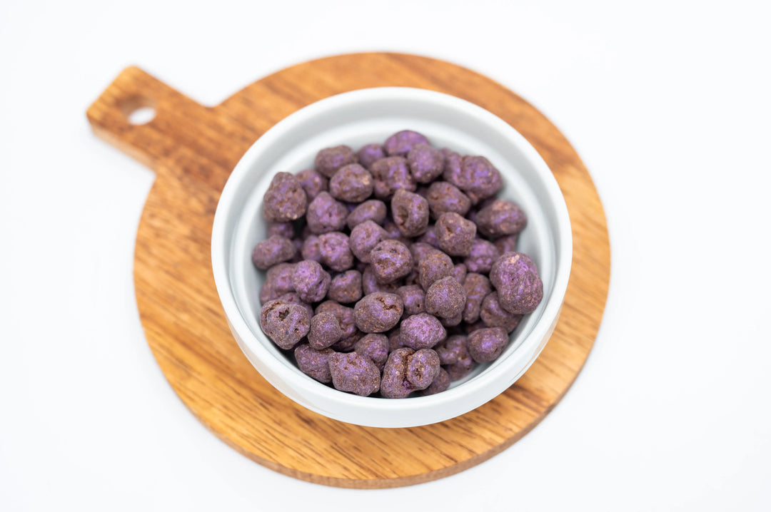 Wooden board holding a white bowl filled with dark chocolate covered blueberries