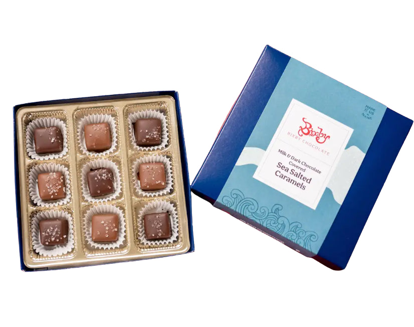 Open 9-piece box of Bixby chocolate caramels in paper cups beside the closed blue gift box