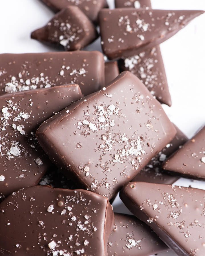 Pile of dark chocolate sea salt toffee pieces on a white background