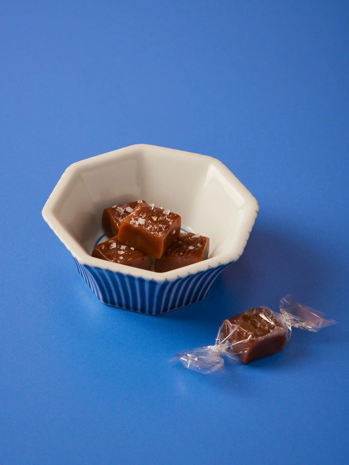 Sea salt caramels in a blue and white bowl with one wrapped caramel beside it