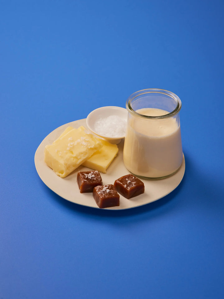 Plate with butter, a small jug of cream and caramels on a blue background