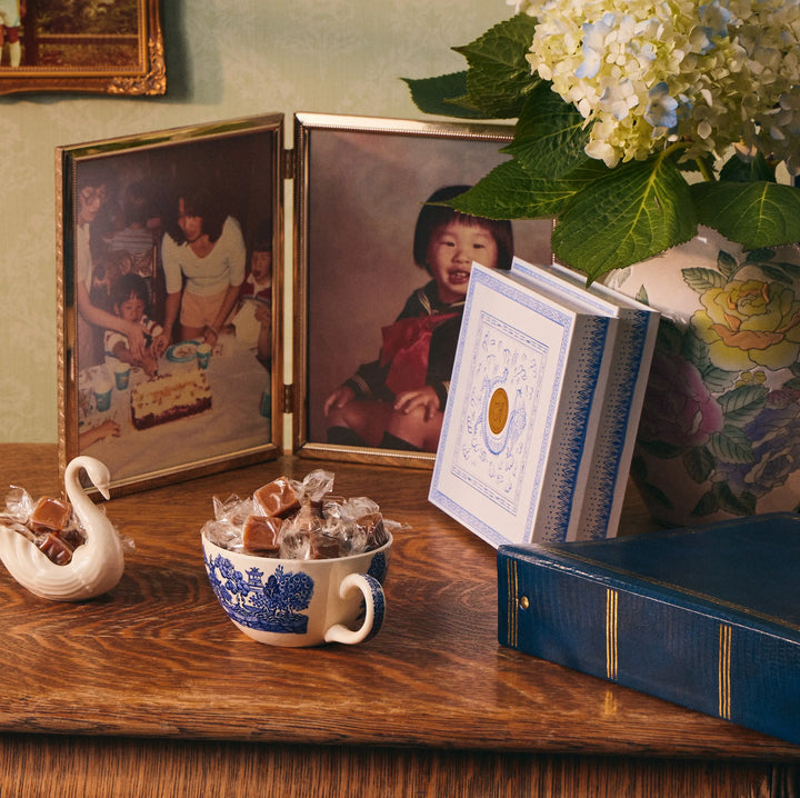 Le Bon Garcon caramel box on a wooden desk beside a teacup of caramels and framed photos
