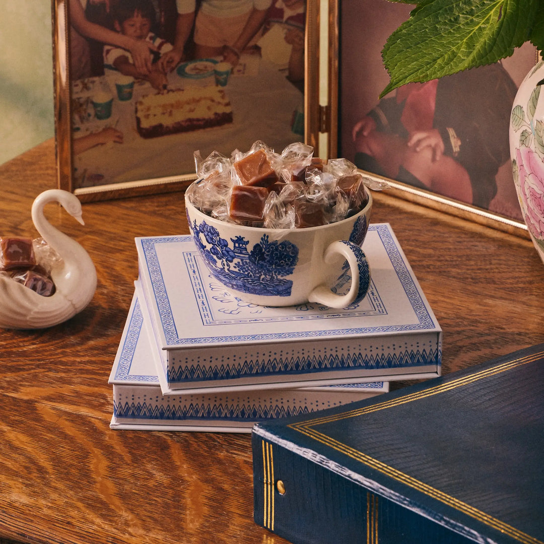 Teacup filled with wrapped caramels resting on stacked Le Bon Garcon gift boxes