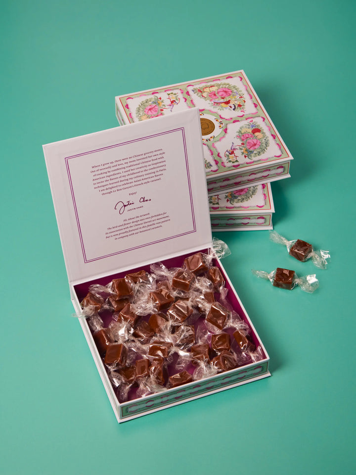 Open pink floral gift box filled with individually wrapped caramels, on a teal background
