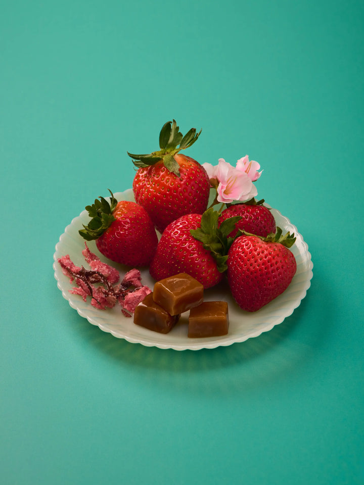 Plate of fresh strawberries and caramels with pink blossoms on a teal background