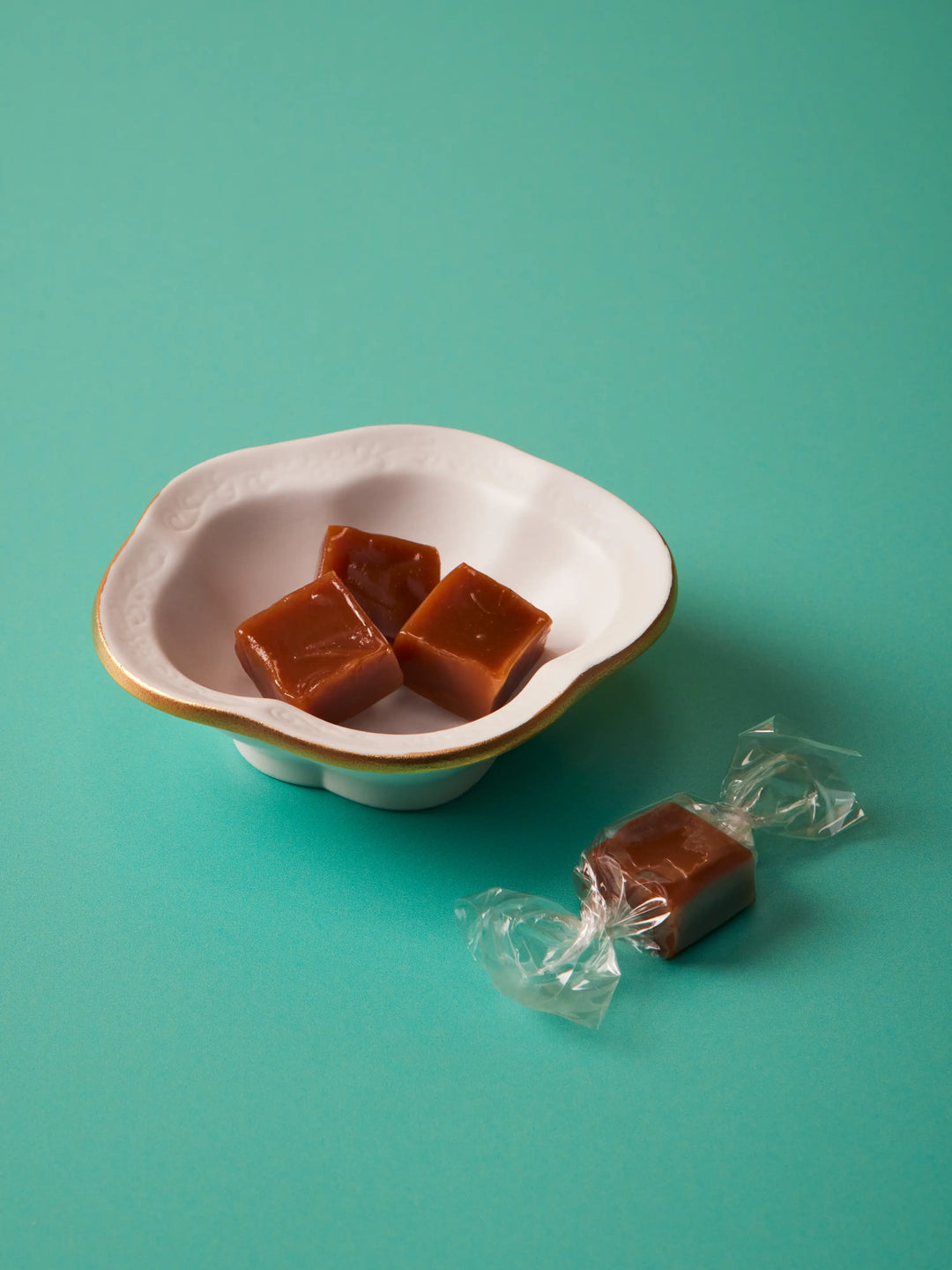Caramels in a white scalloped bowl with a wrapped caramel beside it