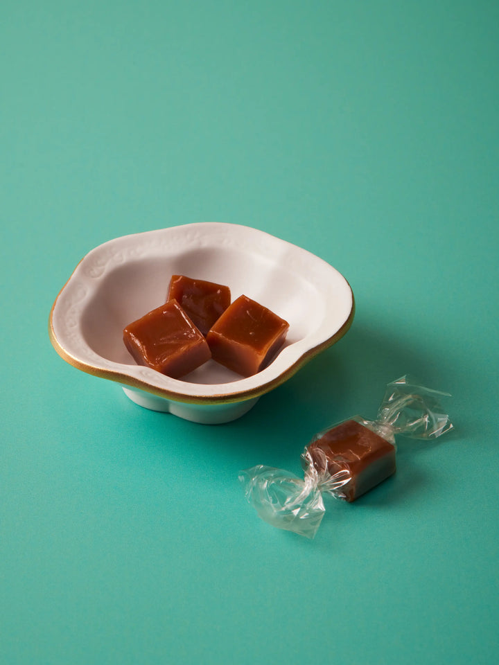 Caramels in a white scalloped bowl with a wrapped caramel beside it