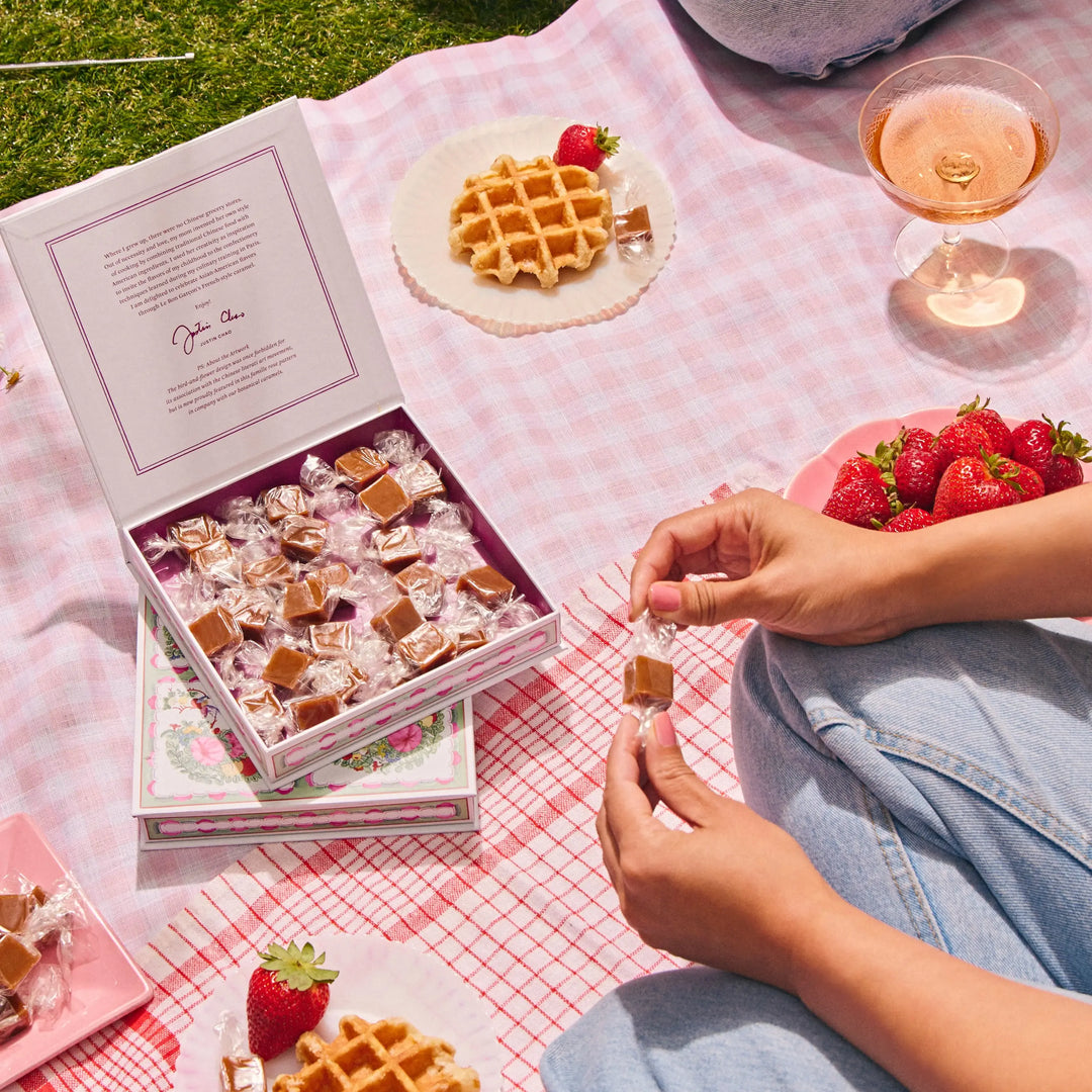 Open box of Strawberry Sakura caramels on a pink gingham picnic blanket with strawberries and waffles
