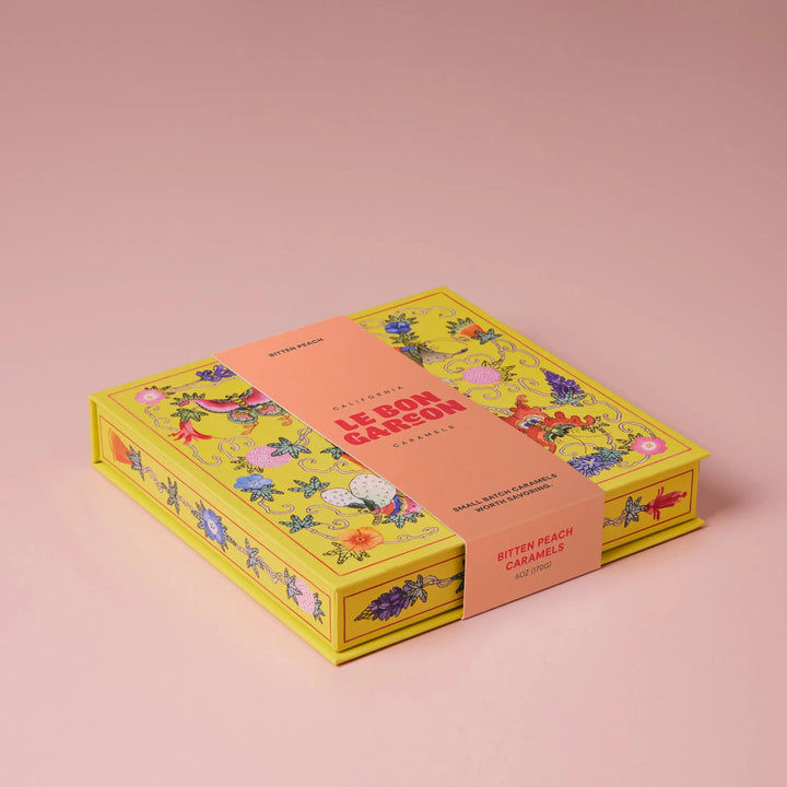 Le Bon Garcon Bitten Peach Caramels gift box in yellow floral print with a peach band, on a pink background