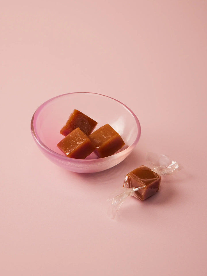 Pink glass bowl of caramels with a wrapped caramel beside it