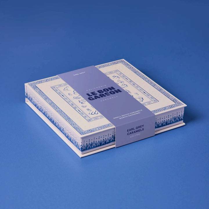 Le Bon Garcon Earl Grey Caramels gift box in blue and white with a lavender band, on a blue background