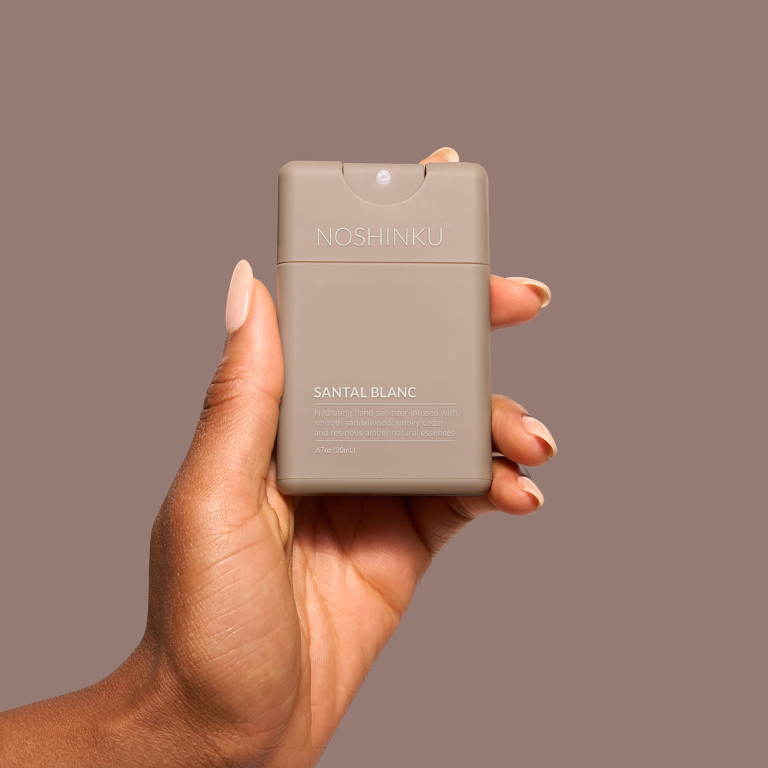 Hand holding the taupe Noshinku pocket sanitizer against a mauve background