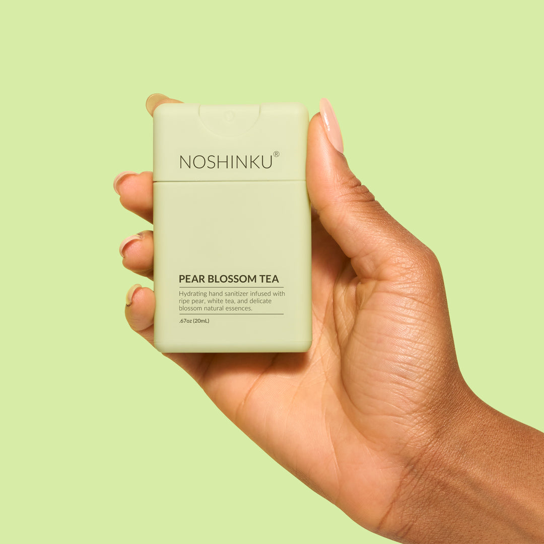 Hand holding the pale green Noshinku pocket sanitizer against a light green background