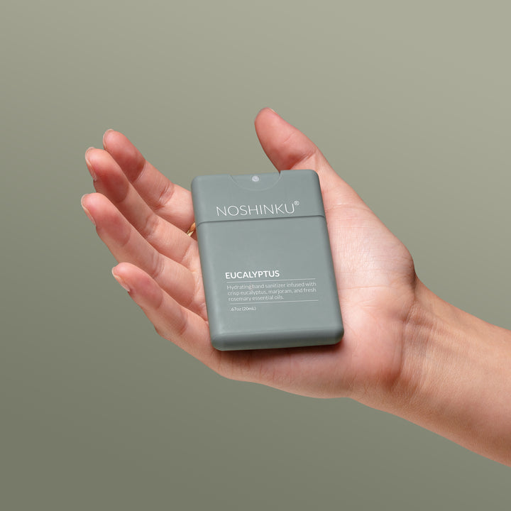 Open hand holding the sage green Noshinku pocket sanitizer