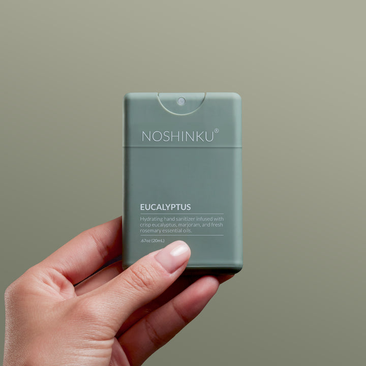 Hand holding the Noshinku Eucalyptus pocket sanitizer against a sage background