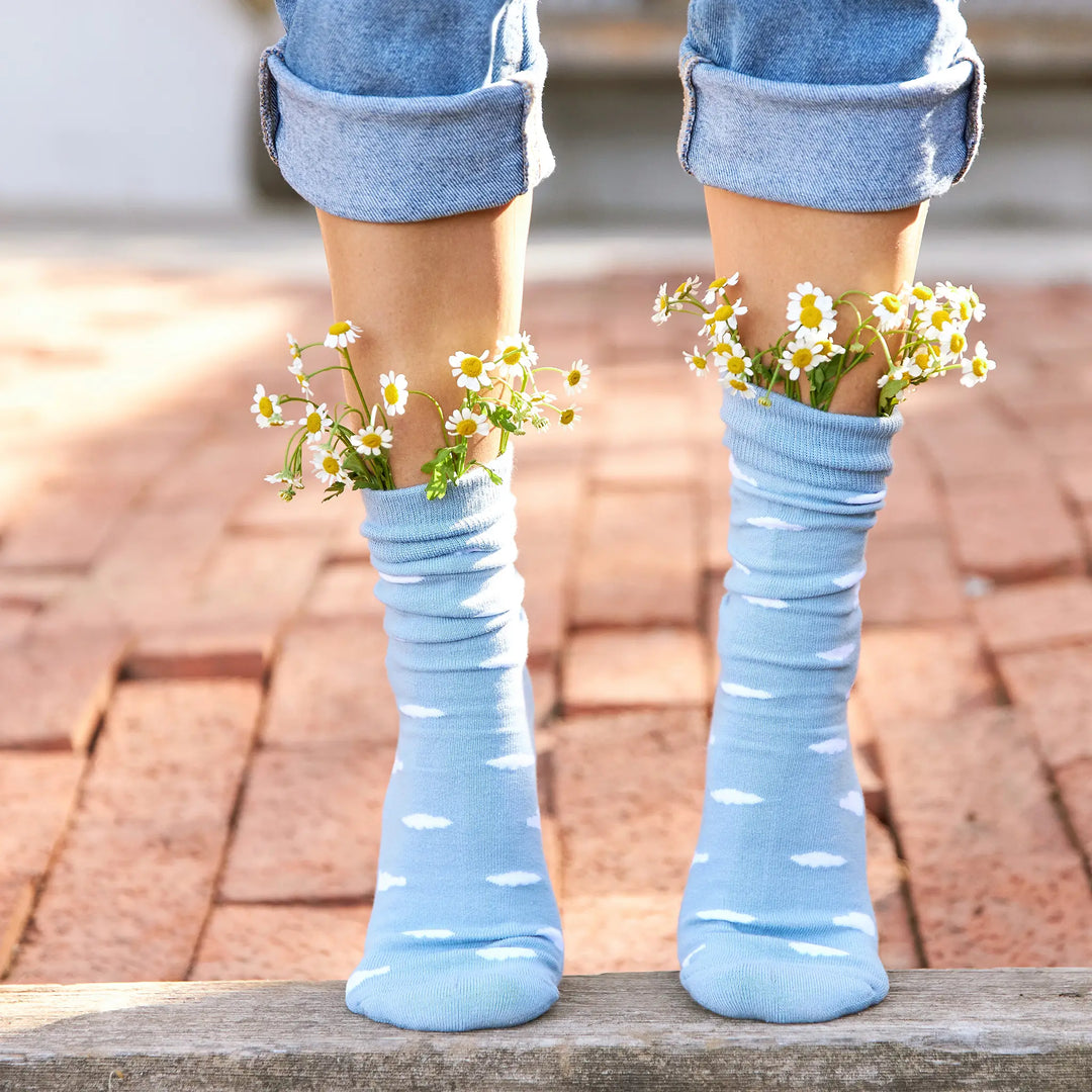 Person wearing light blue socks with small daisies tucked into the cuffs, on a brick path