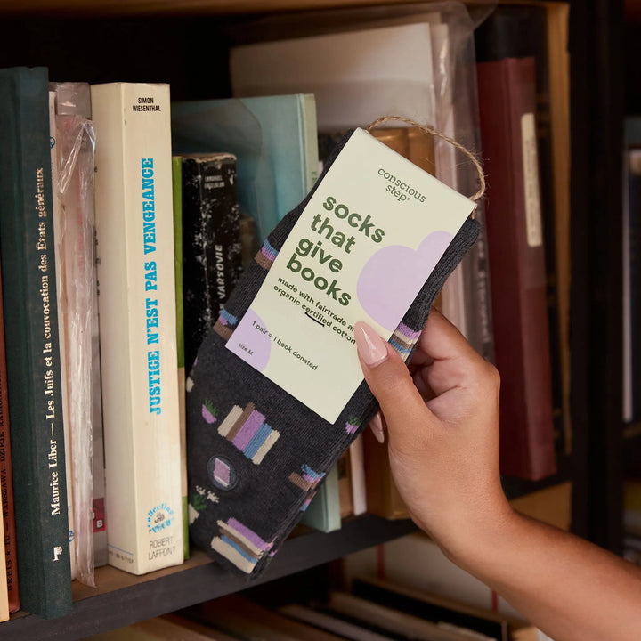 Hand holding tagged Gray Bookshelves socks in front of a bookshelf