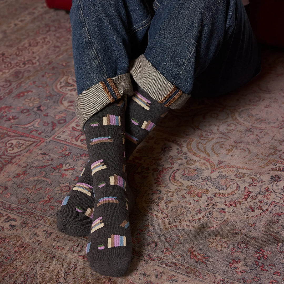 Close view of crossed feet wearing the charcoal bookshelf socks on a patterned rug