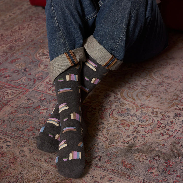 Close view of crossed feet wearing the charcoal bookshelf socks on a patterned rug