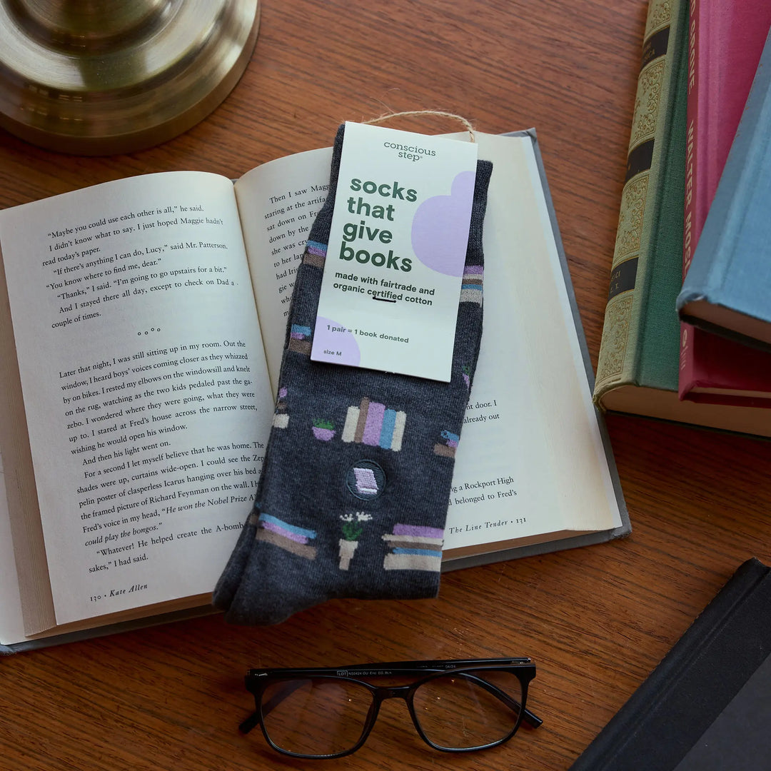 Tagged pair of bookshelf socks resting on an open book beside reading glasses