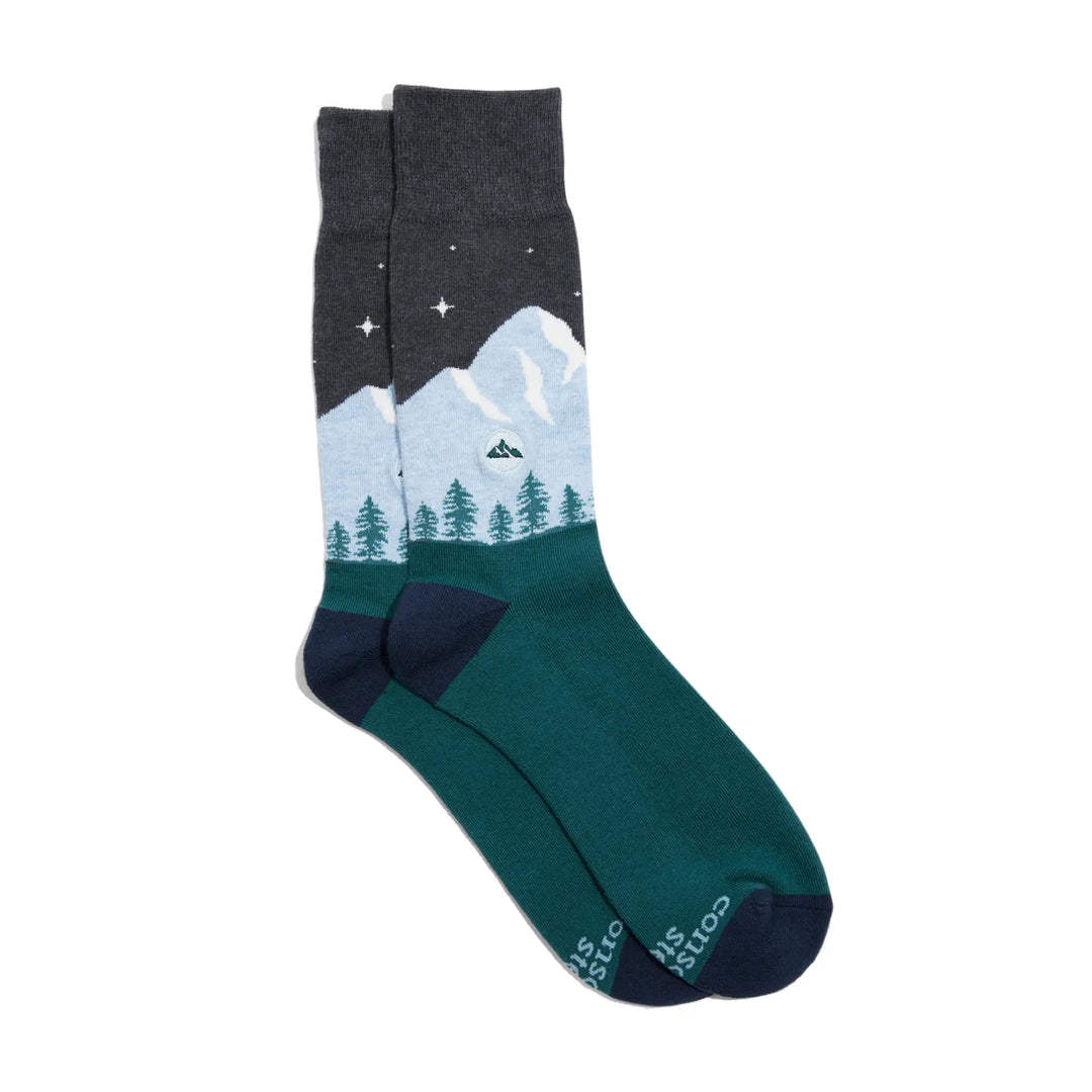 Pair of crew socks with a starry night sky, snowcapped mountains and green evergreen trees