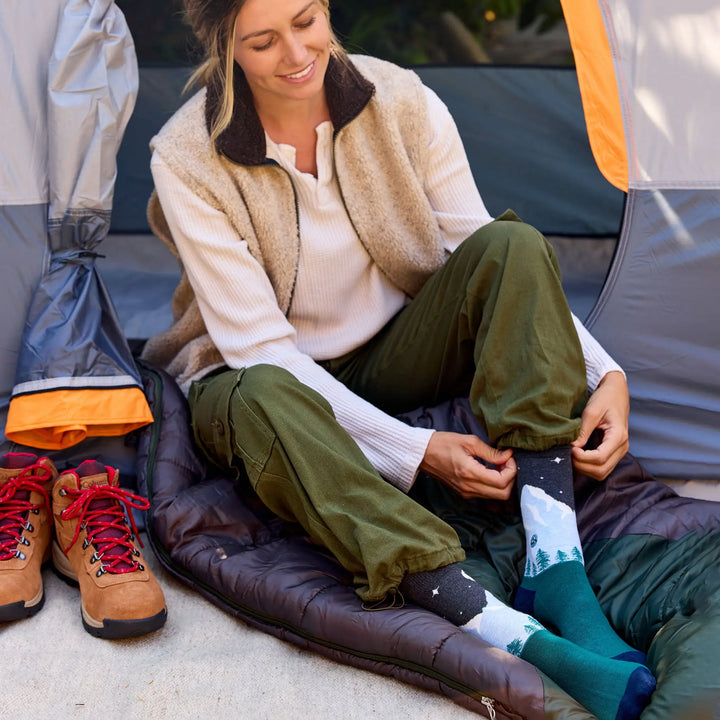 Woman seated in a tent opening pulling on the mountain socks beside hiking boots