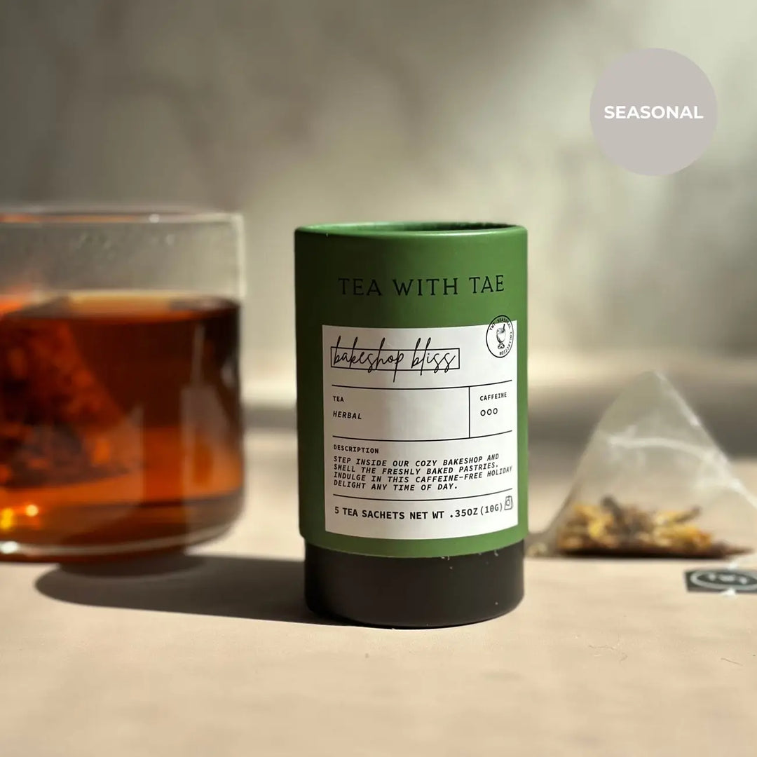 Green Bakeshop Bliss mini tea tube beside a glass of brewed tea and a pyramid sachet