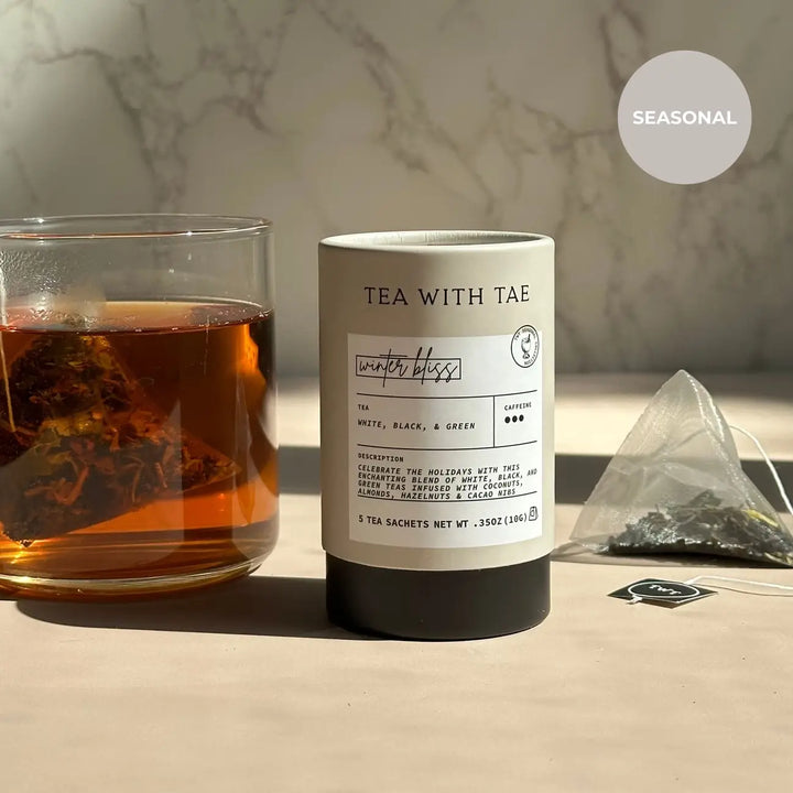 White Winter Bliss mini tea tube beside a glass of brewed tea and a pyramid sachet