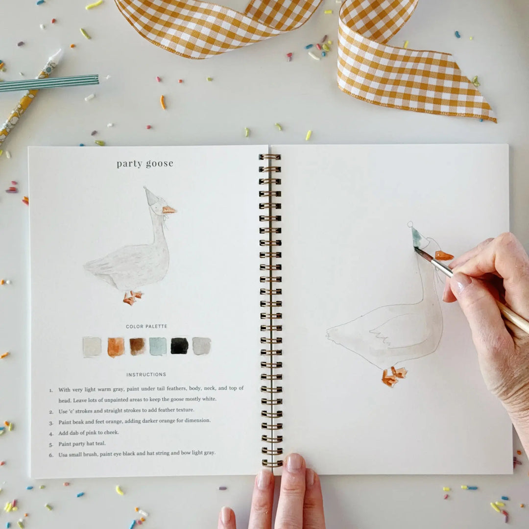 Open workbook with the party goose page, its color palette and step-by-step instructions, and a hand painting the goose